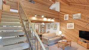 Un intérieur en bois avec un escalier, un canapé, un téléviseur et des tableaux encadrés accrochés aux murs.