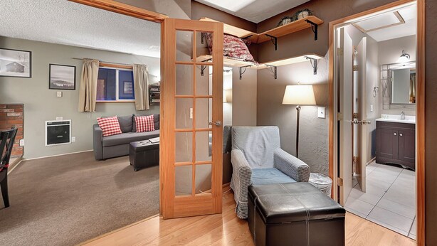 A compact living space with a sofa, ottoman, and a bed with a headboard. A lamp and a small table are also visible.