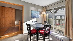 A room with a dining table, chairs, a lamp, and a large window with curtains.