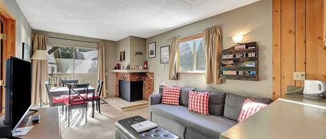 A cozy living room with a fireplace, a sofa with checkered cushions, a coffee table, and a TV.