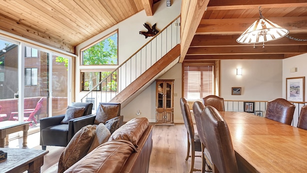 Amplia sala de estar con una escalera de madera, sofás de cuero y una mesa de comedor con sillas.