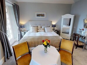 A hotel room with a large bed, a bedside table with a lamp, a desk with a chair, and a window with curtains. - Ranscombe House (Brixham)