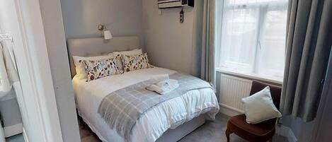 Ein Schlafzimmer mit Bett, Nachttisch, einem Fenster mit Vorhängen und einer Klimaanlage.