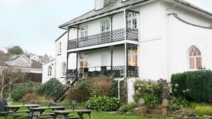 A two-story white building with a balcony, a garden with a picnic table, and a stone wall. - Ranscombe House (Brixham)