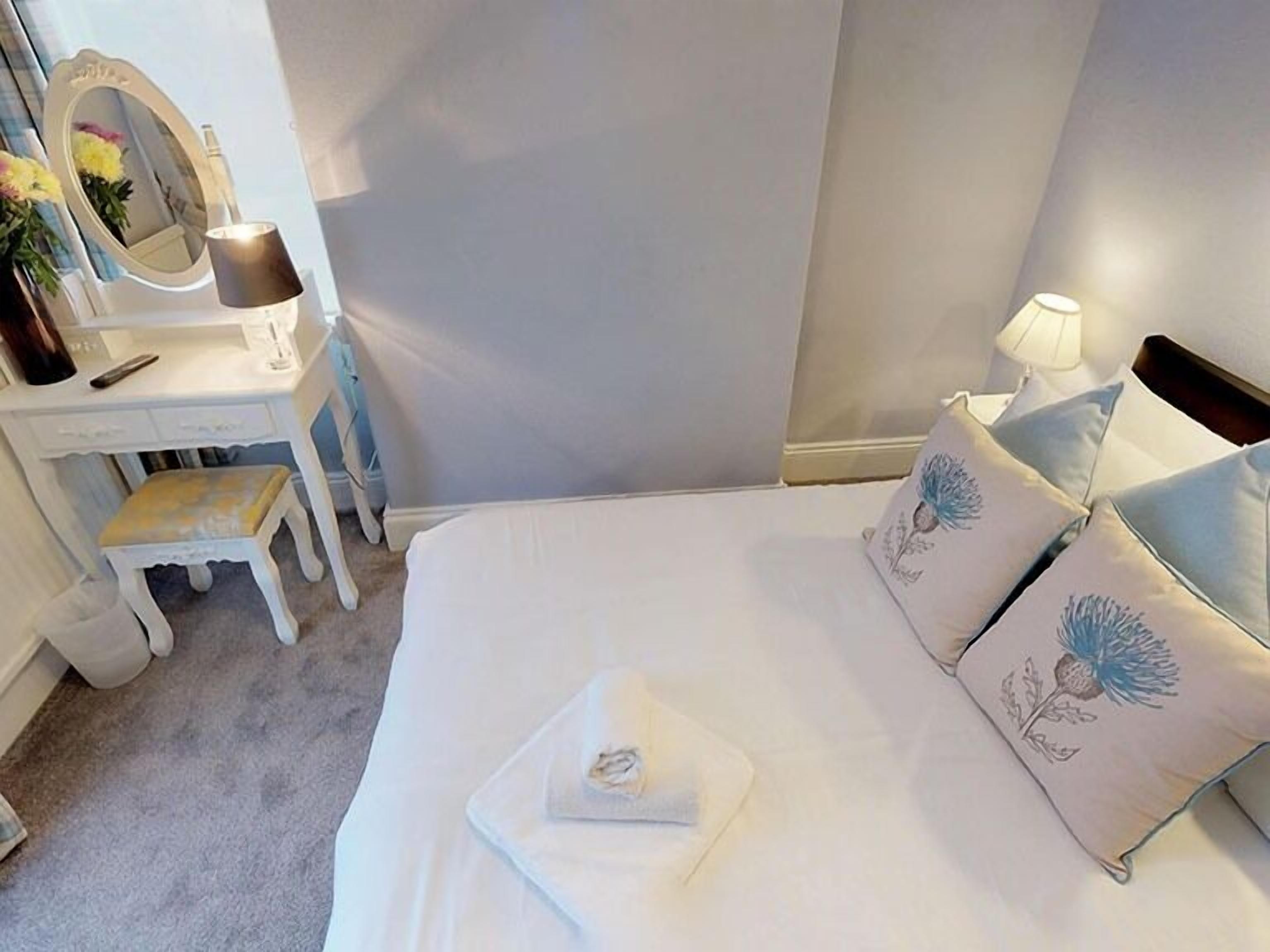 A bedroom with a bed, a bedside table, a mirror, and a lamp.