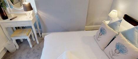 A bedroom with a bed, a bedside table, a mirror, and a lamp.