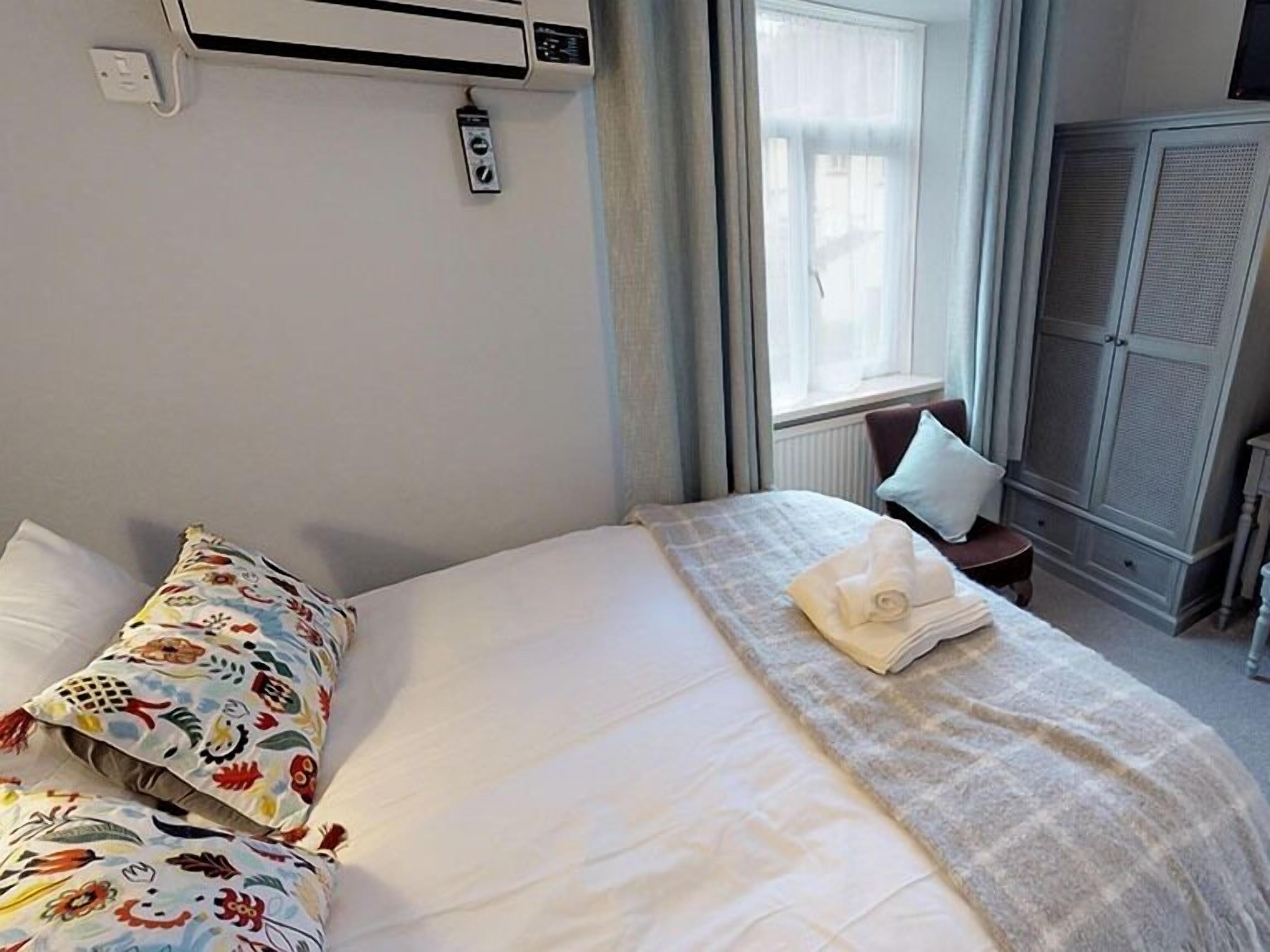 A hotel room with a bed, a window, an air conditioning unit, and a wardrobe.