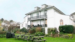 A white building with a balcony and a garden with picnic tables. - Ranscombe House (Brixham)
