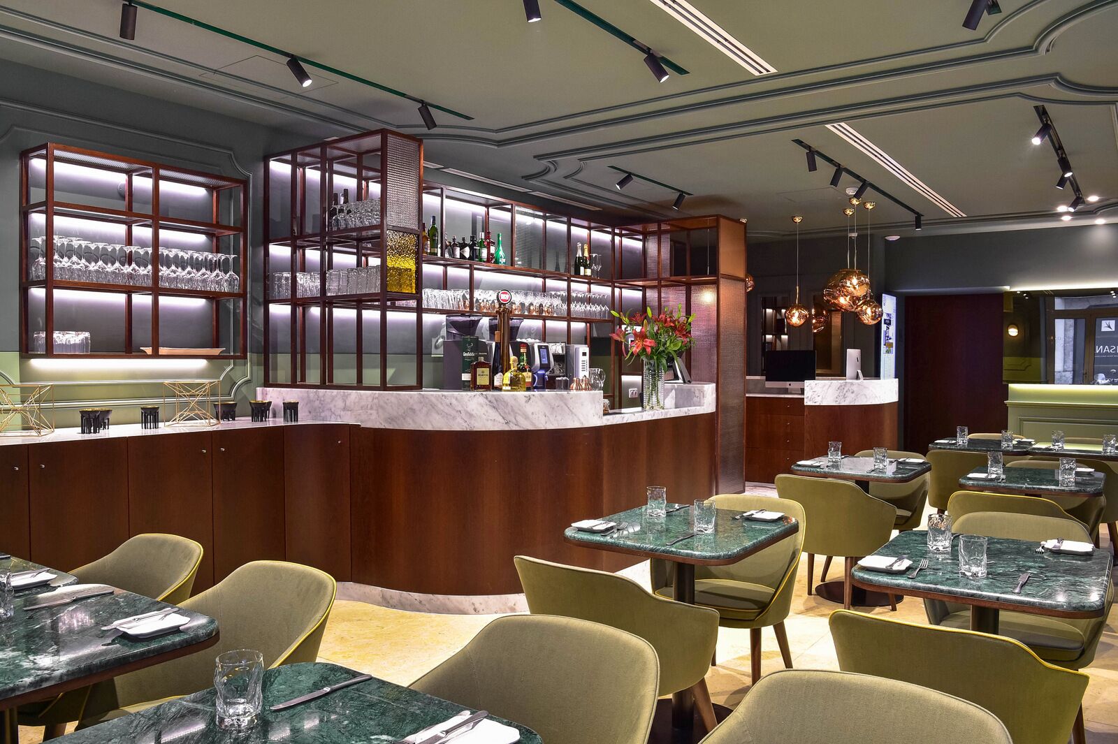 A restaurant with a bar area, marble tables, and cushioned chairs.