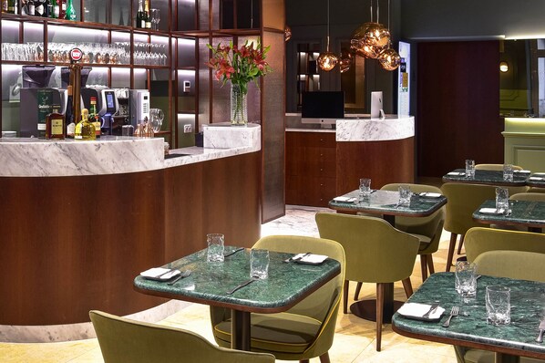A restaurant with a bar area, green marble tables, and yellow chairs. - My Story Hotel Augusta (Lisbon)