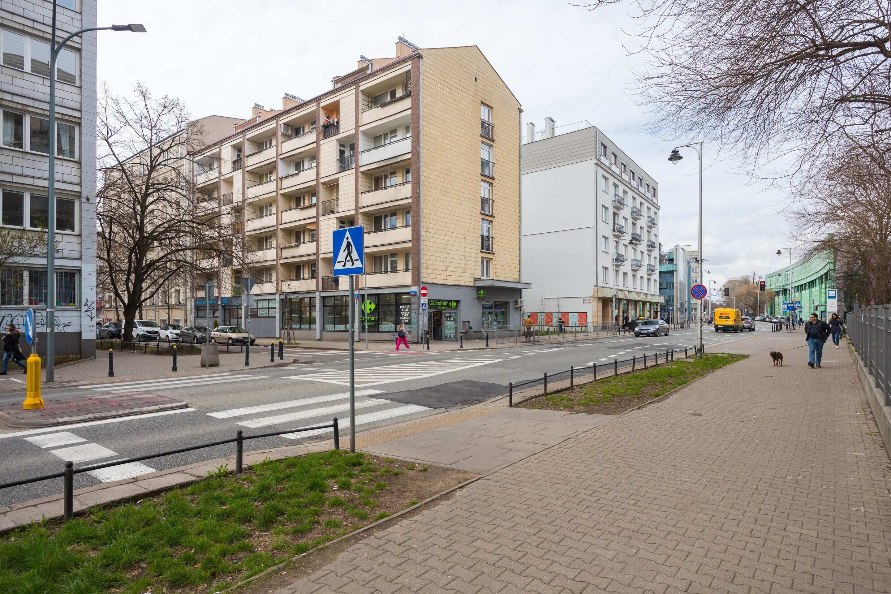 A street view with a pedestrian crossing, buildings, and a sidewalk.
