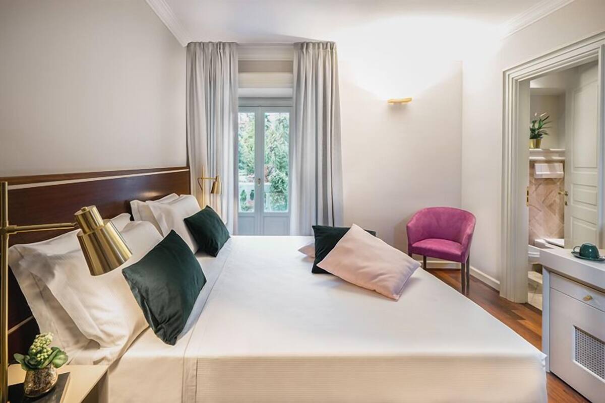 Habitación de hotel con una cama grande, una silla, un escritorio y vistas a zonas verdes.