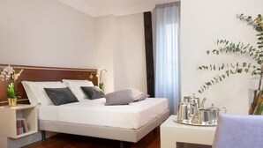 A modern hotel room with a bed, bedside table, and a small desk with a tray of silver items. - Magville (Milan)