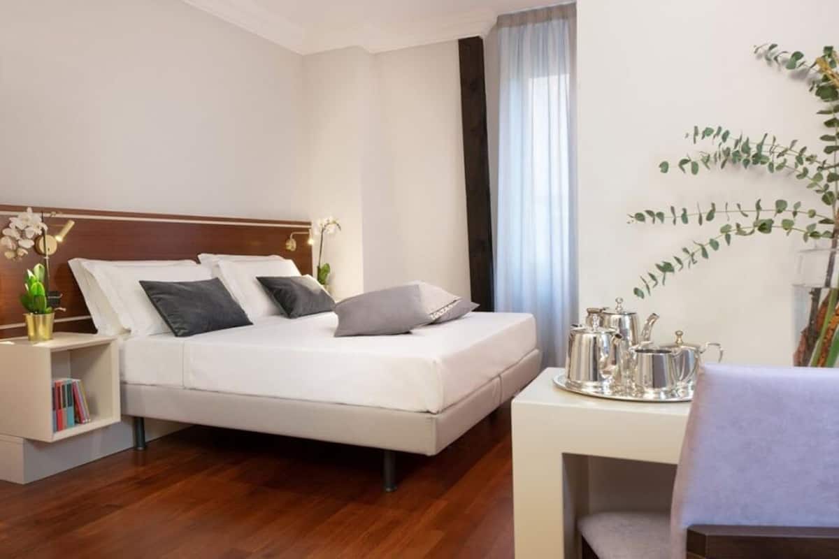 Una habitación de hotel moderna con una cama, una mesita de noche y un pequeño escritorio con una bandeja de objetos de plata.