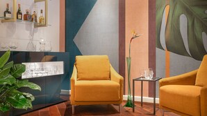 A modern living room with two mustard-colored armchairs, a glass coffee table, a bar area with bottles, and a large abstract painting on the wall. - Magville (Milan)