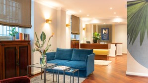A modern living room with a blue sofa, a glass coffee table, and a wooden cabinet. There is a reception desk with a sign that reads "MAG VILLE". - Magville (Milan)