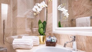 A bathroom with a marble sink, a gold vase with a plant, and white towels. - Magville (Milan)