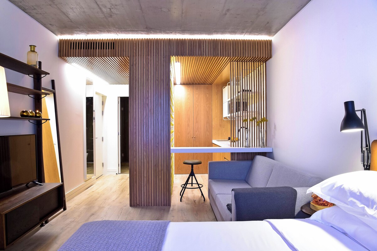 Quarto de hotel moderno com cama, escrivaninha e área de estar.