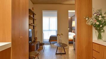 A modern room with a wooden floor, a bed with a gray headboard, a desk with a chair, and a small table with a vase of flowers.