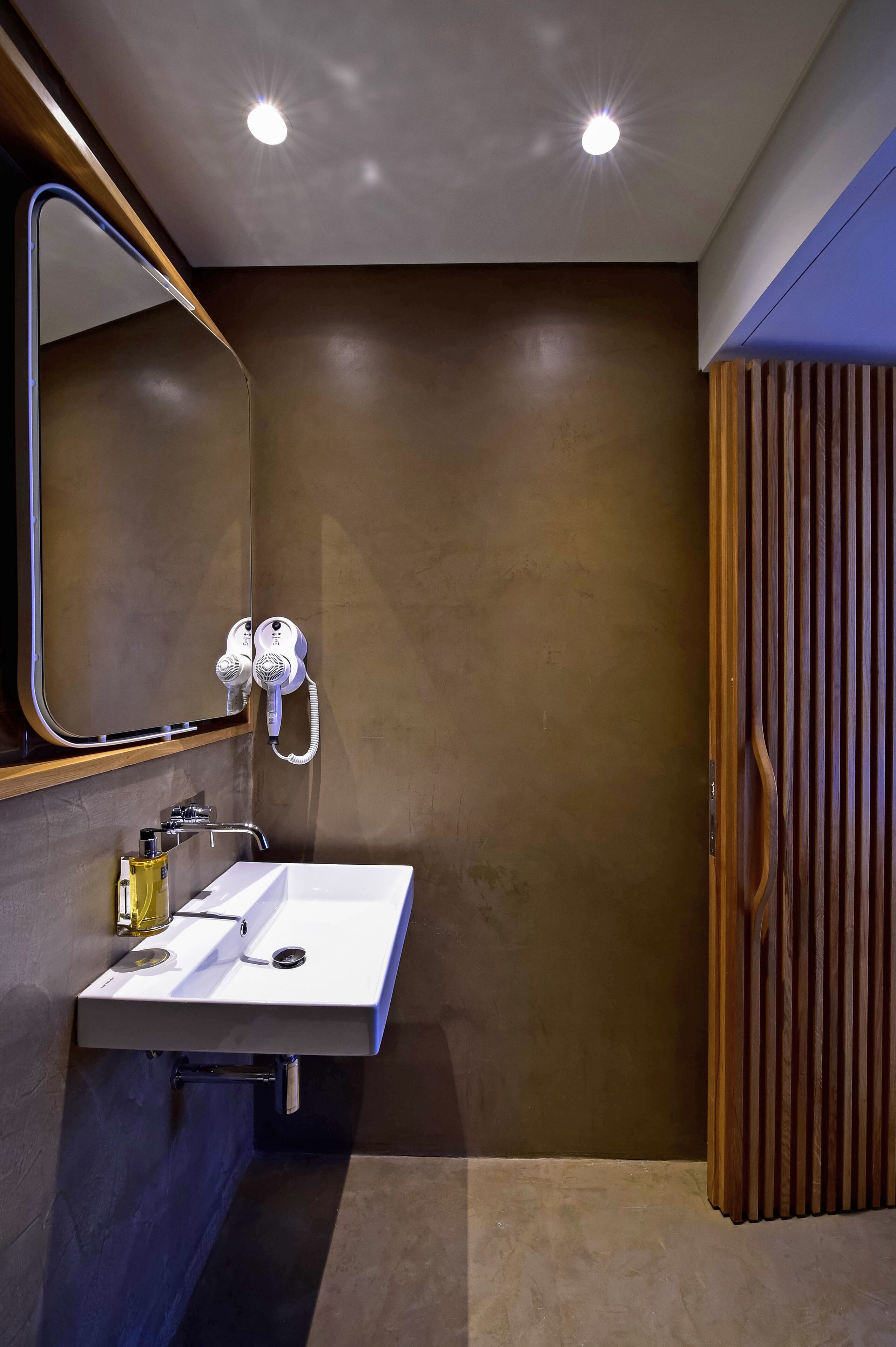 A modern bathroom with a white sink, a mirror, and a hairdryer mounted on the wall.