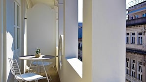 A small balcony with a round table and two chairs, a potted plant, and a view of a building with balconies. - My Story Apartments Porto - Santa Catarina (Porto)