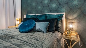 A neatly made bed with a quilted cover, multiple pillows, and a bedside table with a lamp and a decorative item. - Mennica Residence Chic Apartment (Warsaw)