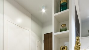 A hallway with a white door, a brown door, and a white shelving unit with decorative items. - Mennica Residence Chic Apartment (Warsaw)
