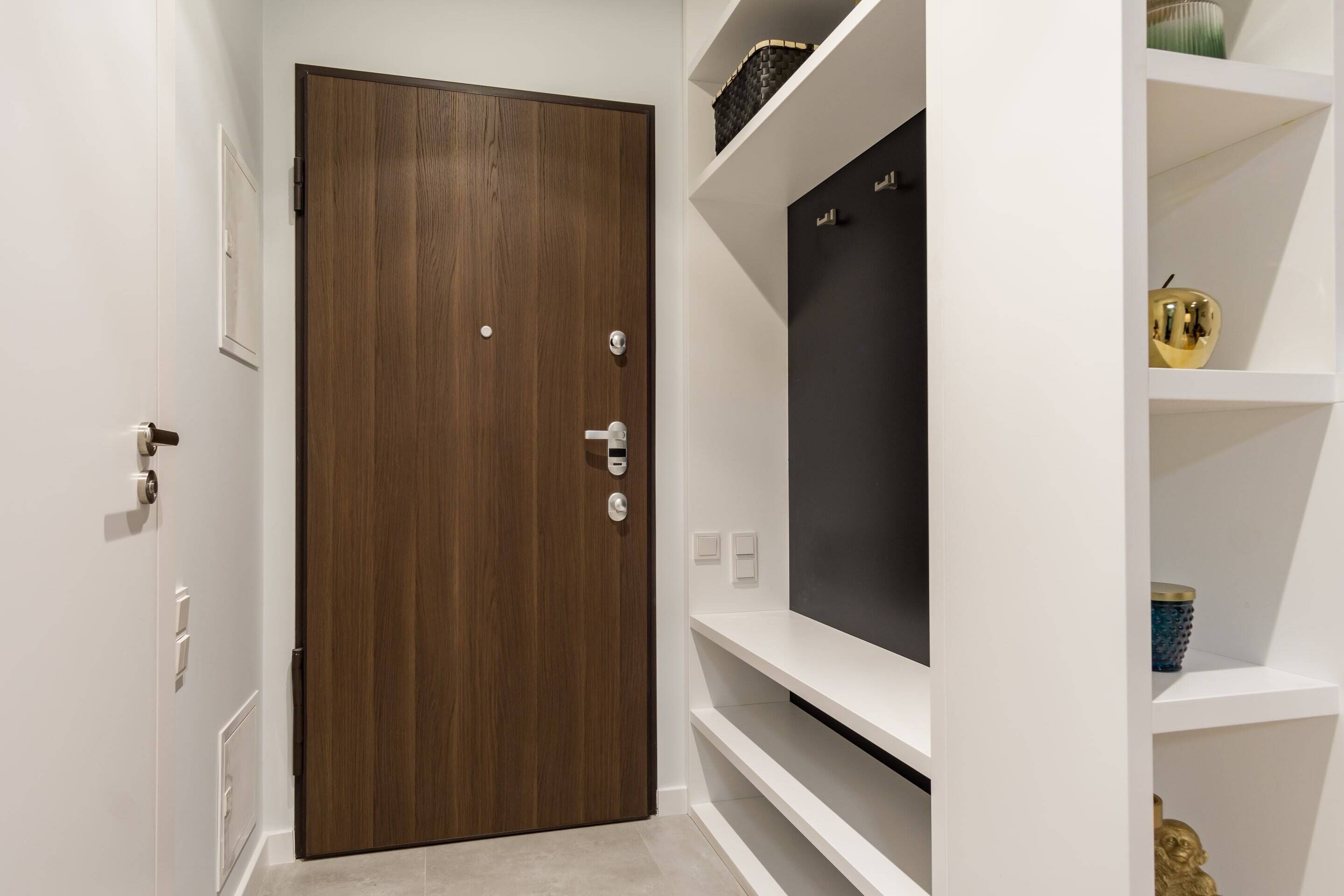 Una habitación moderna con puerta de madera, paredes blancas y una estantería negra con objetos decorativos.
