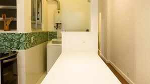 A modern kitchen with a white countertop, a built-in oven, a washing machine, and a hanging light fixture. - Omar do Rio - SL109 (Rio de Janeiro)