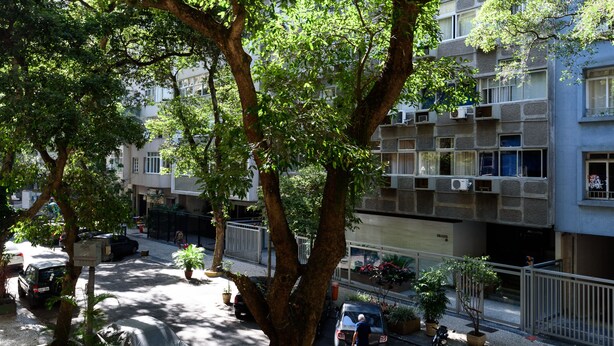 A tree-lined street with a building featuring multiple balconies and air conditioning units. - Omar do Rio - SL109 (Rio de Janeiro)
