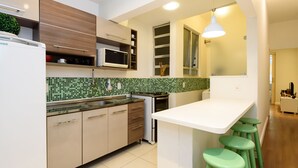A modern kitchen with a white countertop, green stools, and a microwave. - Omar do Rio - SL109 (Rio de Janeiro)