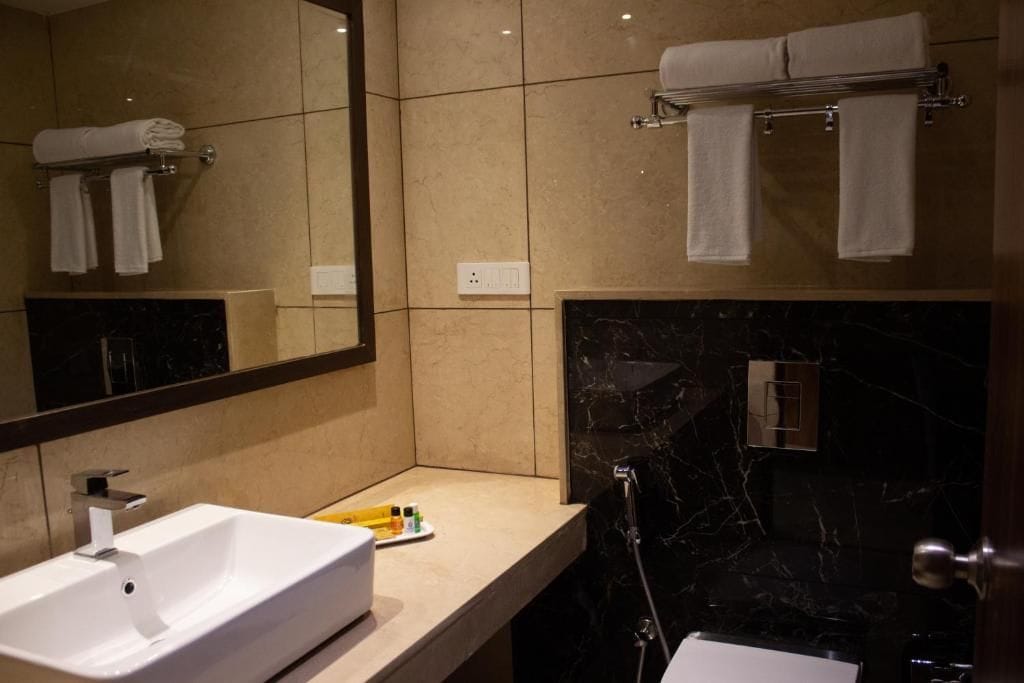 A modern bathroom with a white sink, a mirror, and a black marble shower area.