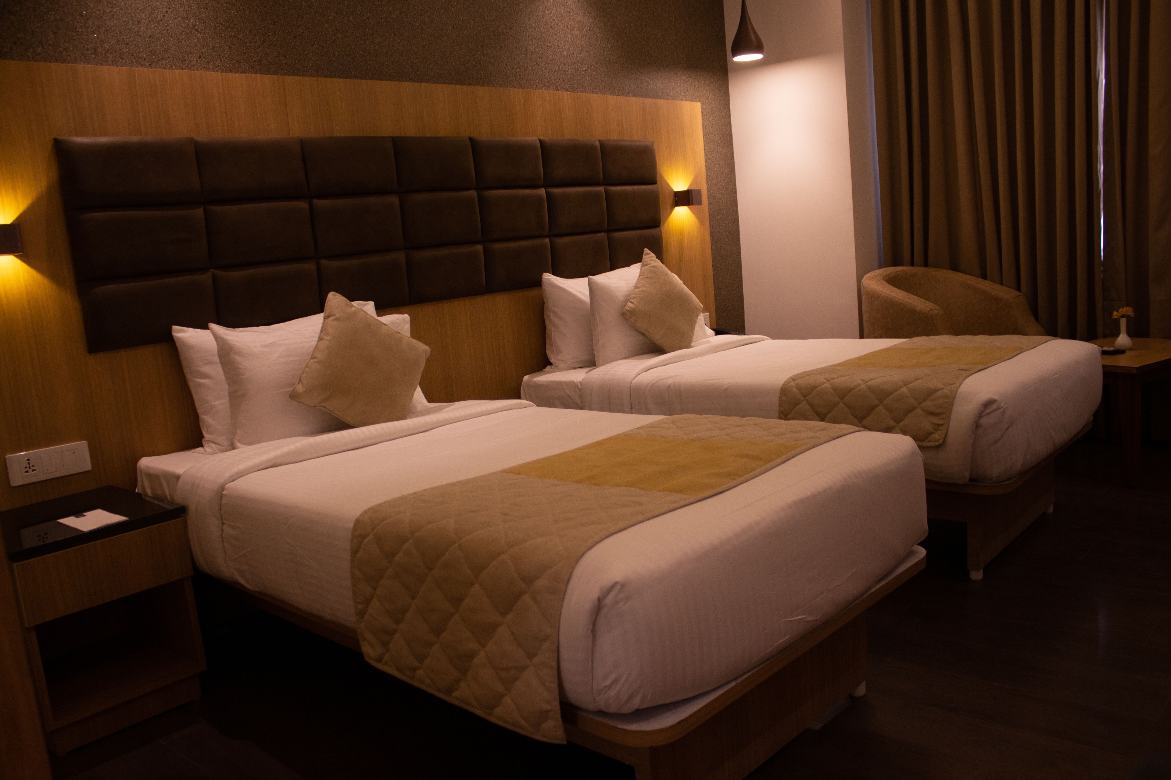 Una habitación de hotel con dos camas, cabecera de madera, mesita de noche y una silla.