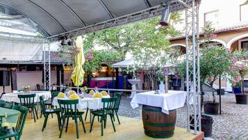 Un área de comedor al aire libre con mesas y sillas, un escenario y un fondo decorativo.