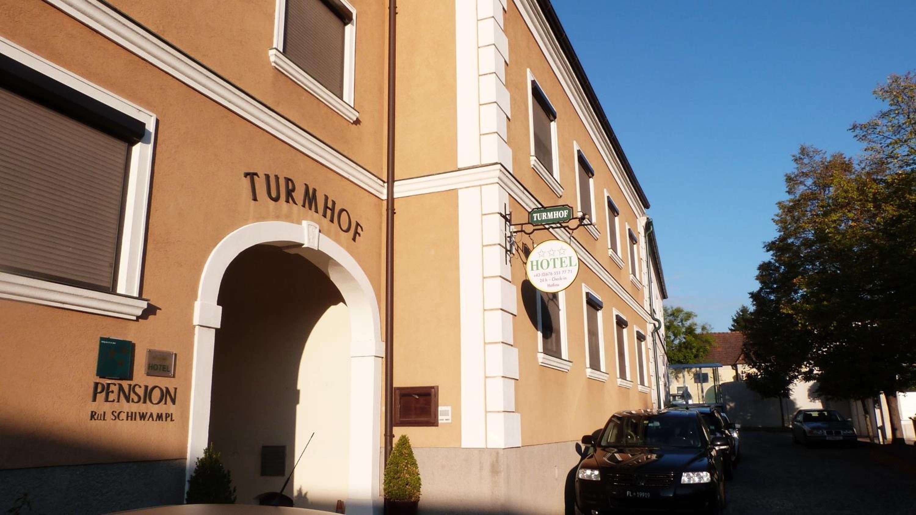 Un edificio con una entrada en arco con la leyenda 'TURNHOF' y un cartel que indica 'HOTEL' con información de contacto.
