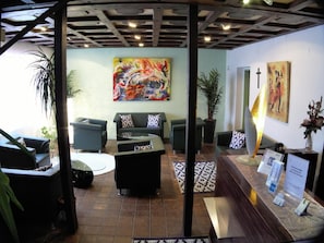 A lobby with a sofa, chairs, a coffee table, a painting, a cross, and a sign.