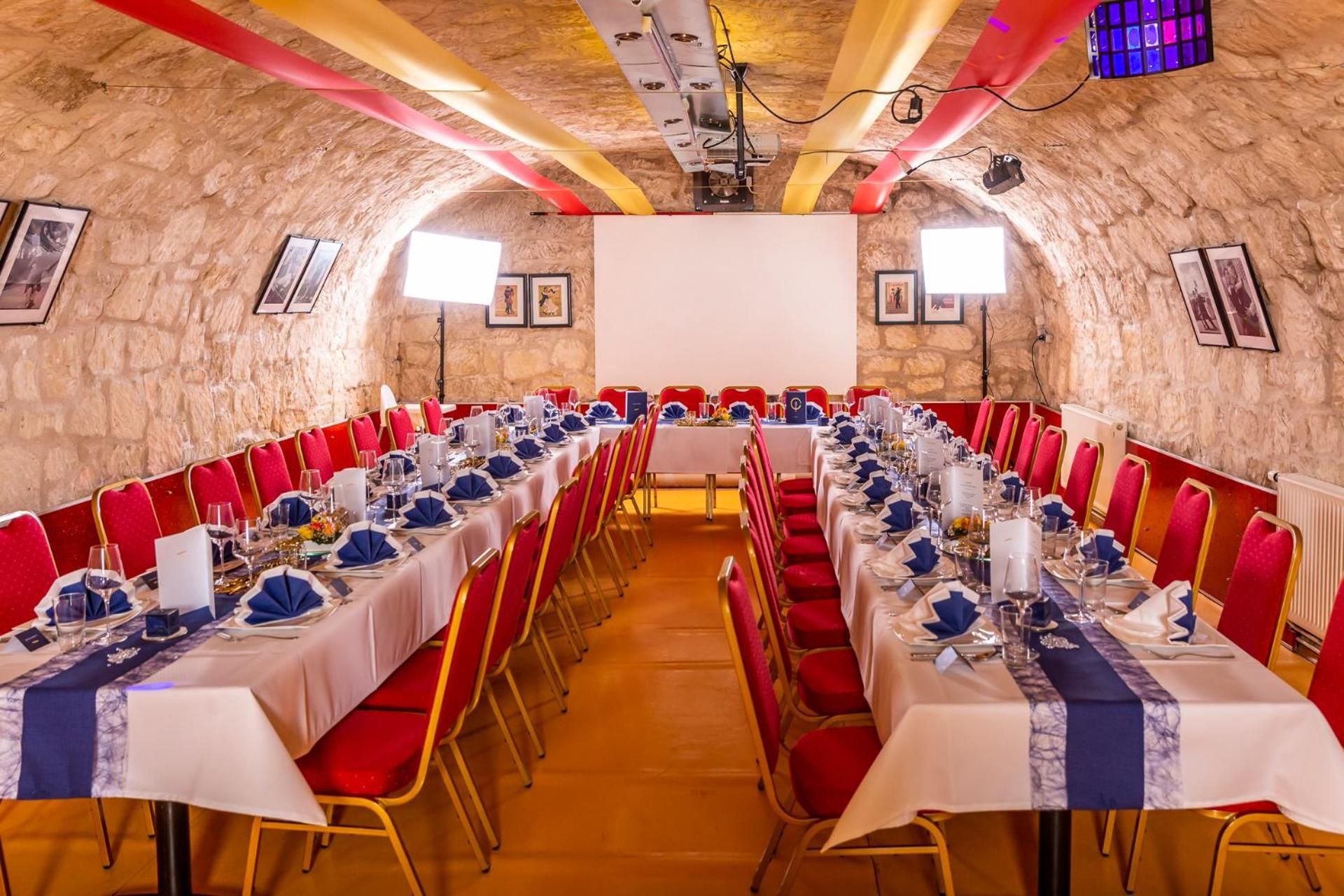 A conference room with long tables, red chairs, and a projector screen.