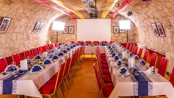Un salón de conferencias con mesas largas, sillas rojas y una pantalla para proyector.