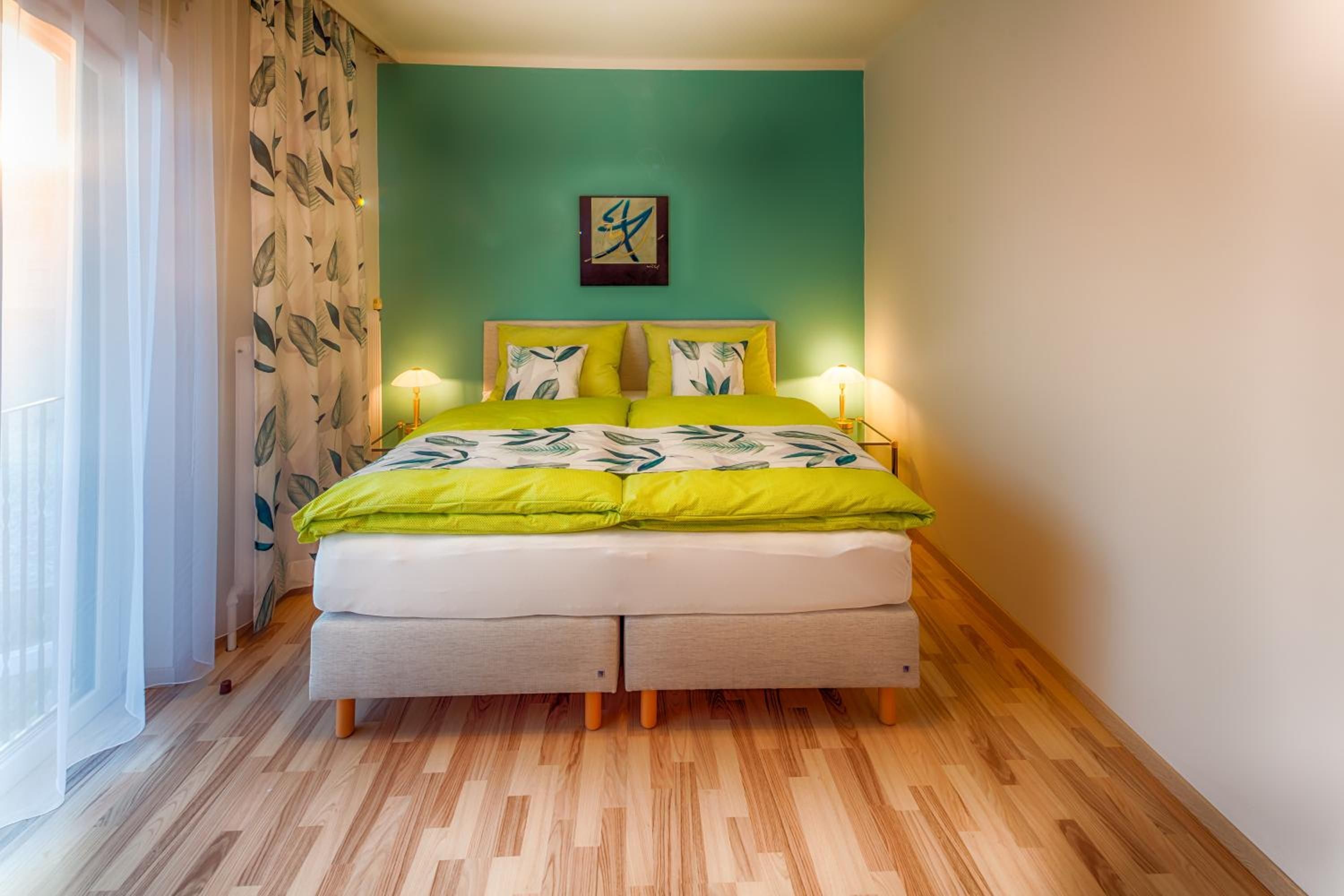 Een slaapkamer met een bed, nachtkastje, lamp en een raam met gordijnen.