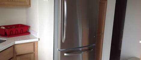 A stainless steel refrigerator in a kitchen with wooden cabinets and a red dish rack on the counter.