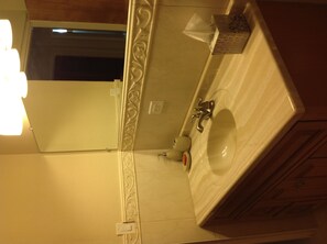 A bathroom with a mirror, sink, and wooden cabinets. - Central Apartment (Devonshire Parish)