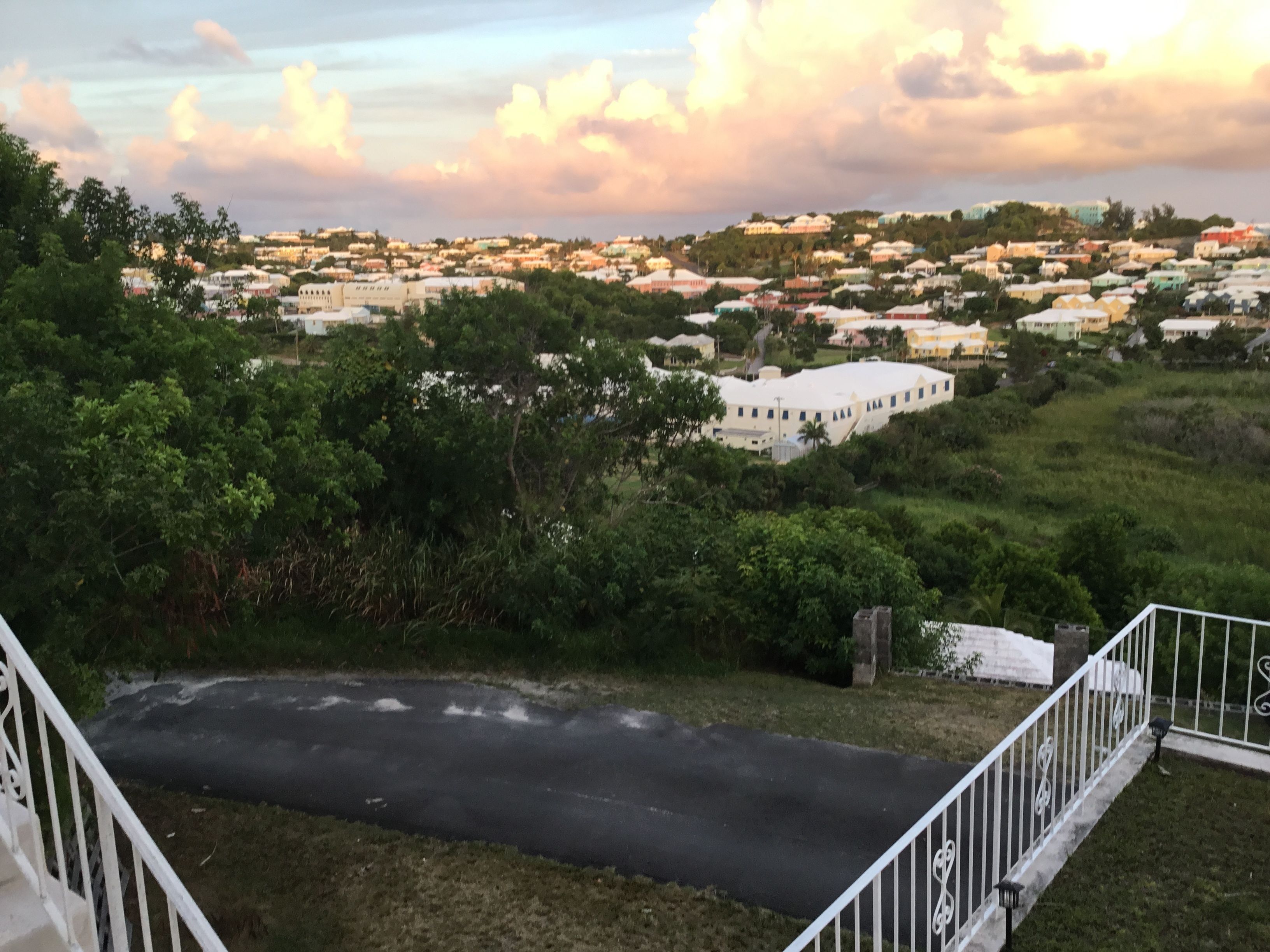 A residential area with houses and greenery, a paved road, and a white building with a flat roof.