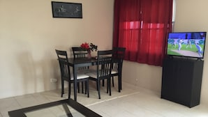 A living room with a dining table, chairs, a TV, and a framed picture on the wall. - Central Apartment (Devonshire Parish)