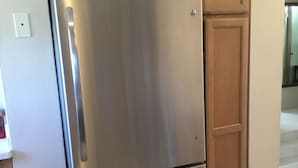 A stainless steel refrigerator in a kitchen with wooden cabinets. - Central Apartment (Devonshire Parish)