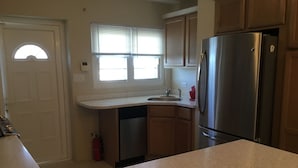 A kitchen with a stainless steel refrigerator, a dishwasher, wooden cabinets, a window with blinds, and a door with a semi-circular window. - Central Apartment (Devonshire Parish)
