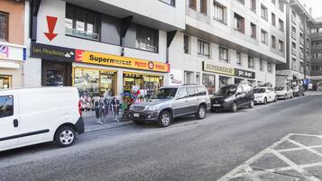 A street view with a row of parked cars and a building with a 'Supermercat' sign.