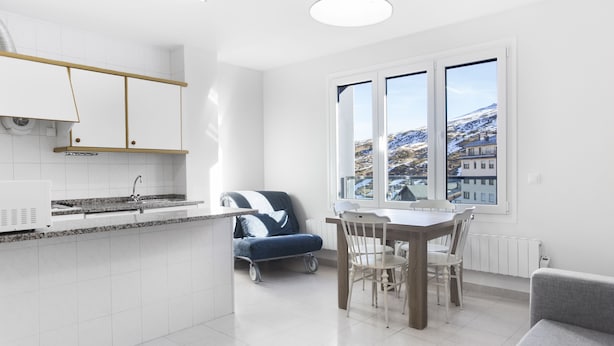Een moderne keuken met witte kasten, een granieten aanrechtblad en een eethoek met een tafel en stoelen.