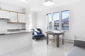 A modern kitchen with white cabinets, a granite countertop, and a dining area with a table and chairs. - Abelletes Apartments (Pas de la Casa)