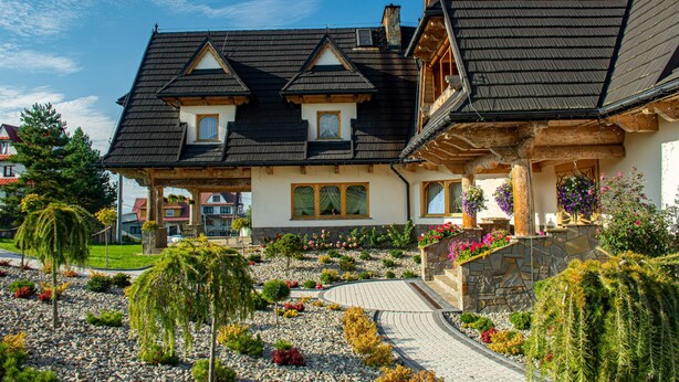 Un chalet traditionnel avec une façade en pierre, un toit à pente et un jardin aménagé, agrémenté d’un sentier menant à l’entrée.