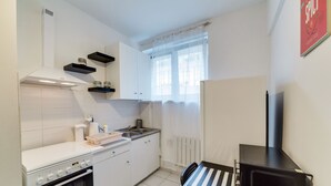 A compact kitchen with white cabinets, a stove, and a microwave. - Dream Loft Łagiewniki (Gdansk)